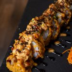 Un plato de sushi con roles tempurizados y topping de camarones.