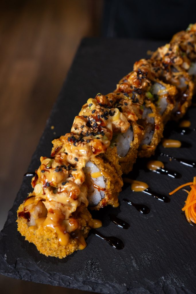Un plato de sushi con roles tempurizados y topping de camarones.