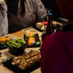 Grupo de personas disfrutando sushi en Sudoki Sushi & Fusion Barcelona, con edamame, nigiris y rollos tempura sobre la mesa durante una cena de empresa.