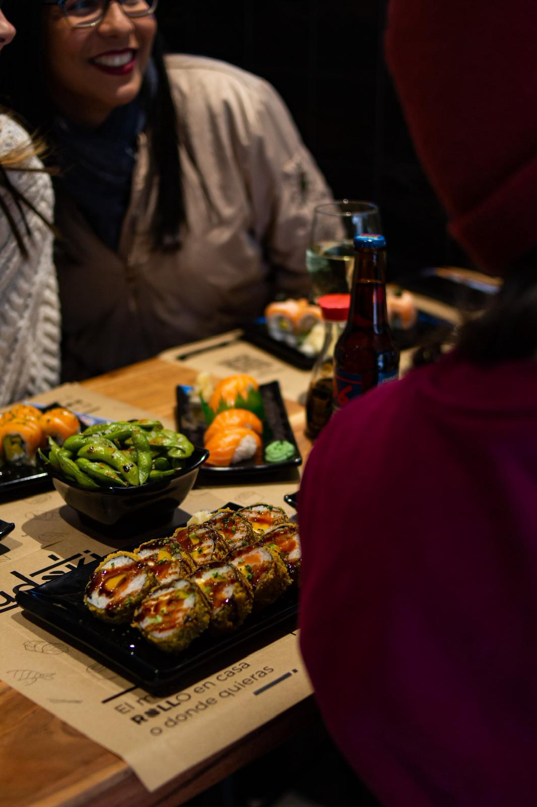 Grupo de personas disfrutando sushi en Sudoki Sushi & Fusion Barcelona, con edamame, nigiris y rollos tempura sobre la mesa durante una cena de empresa.