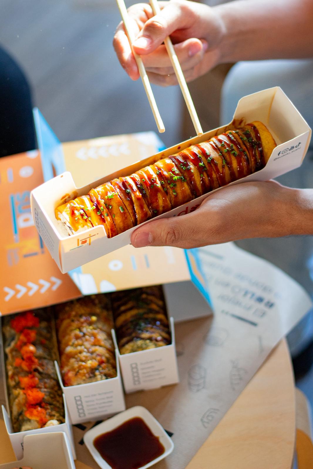 Caja de Sushi Box Sudoki Sushi & Fusion Barcelona para delivery, con rollos tempura, salsa teriyaki y topping crujiente, lista para disfrutar en casa.