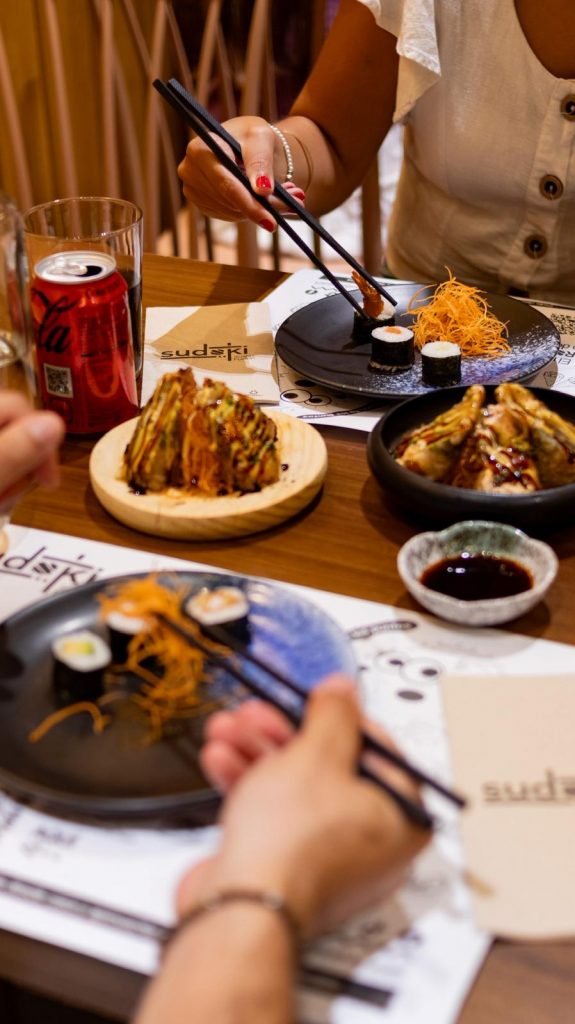 Pareja disfrutando del menú de mediodía en Sudoki Sushi & Fusion Barcelona, con gyozas, makis y refrescos en mesa del restaurante del Eixample.