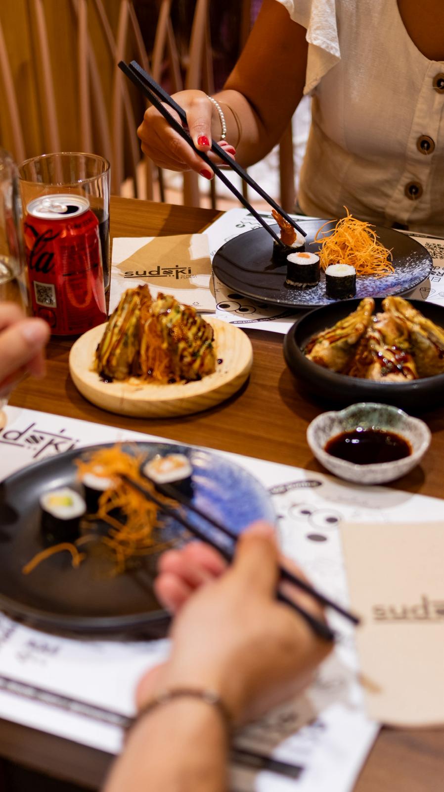 Pareja disfrutando del menú de mediodía en Sudoki Sushi & Fusion Barcelona, con gyozas, makis y refrescos en mesa del restaurante del Eixample.
