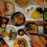 Mesa con variedad de platos del buffet a la carta de sushi de Sudoki en Barcelona, con sushi, gyozas, noodles y comida asiática fusión latina recién preparada.