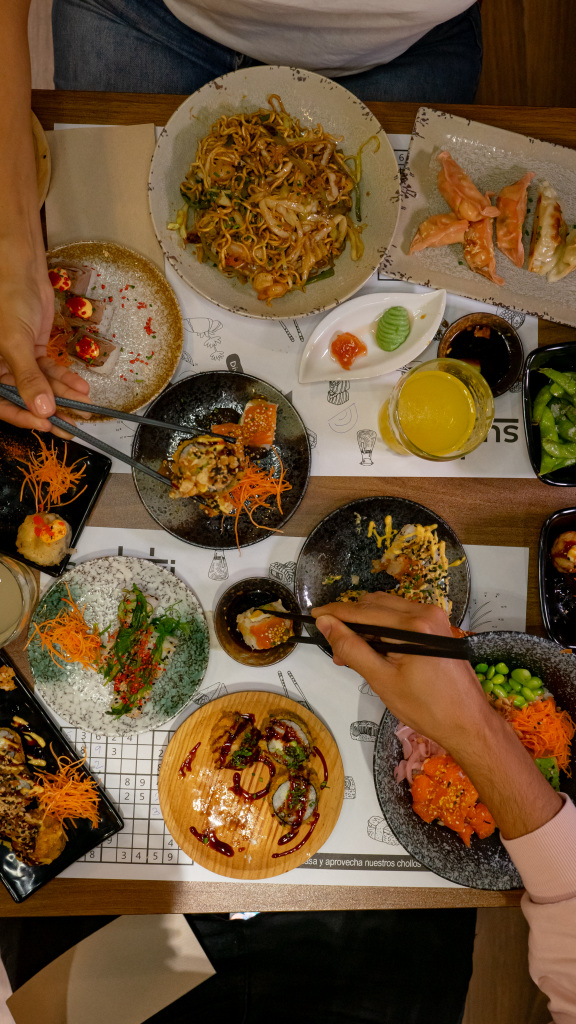 Mesa con variedad de platos del buffet a la carta de sushi de Sudoki en Barcelona, con sushi, gyozas, noodles y comida asiática fusión latina recién preparada.